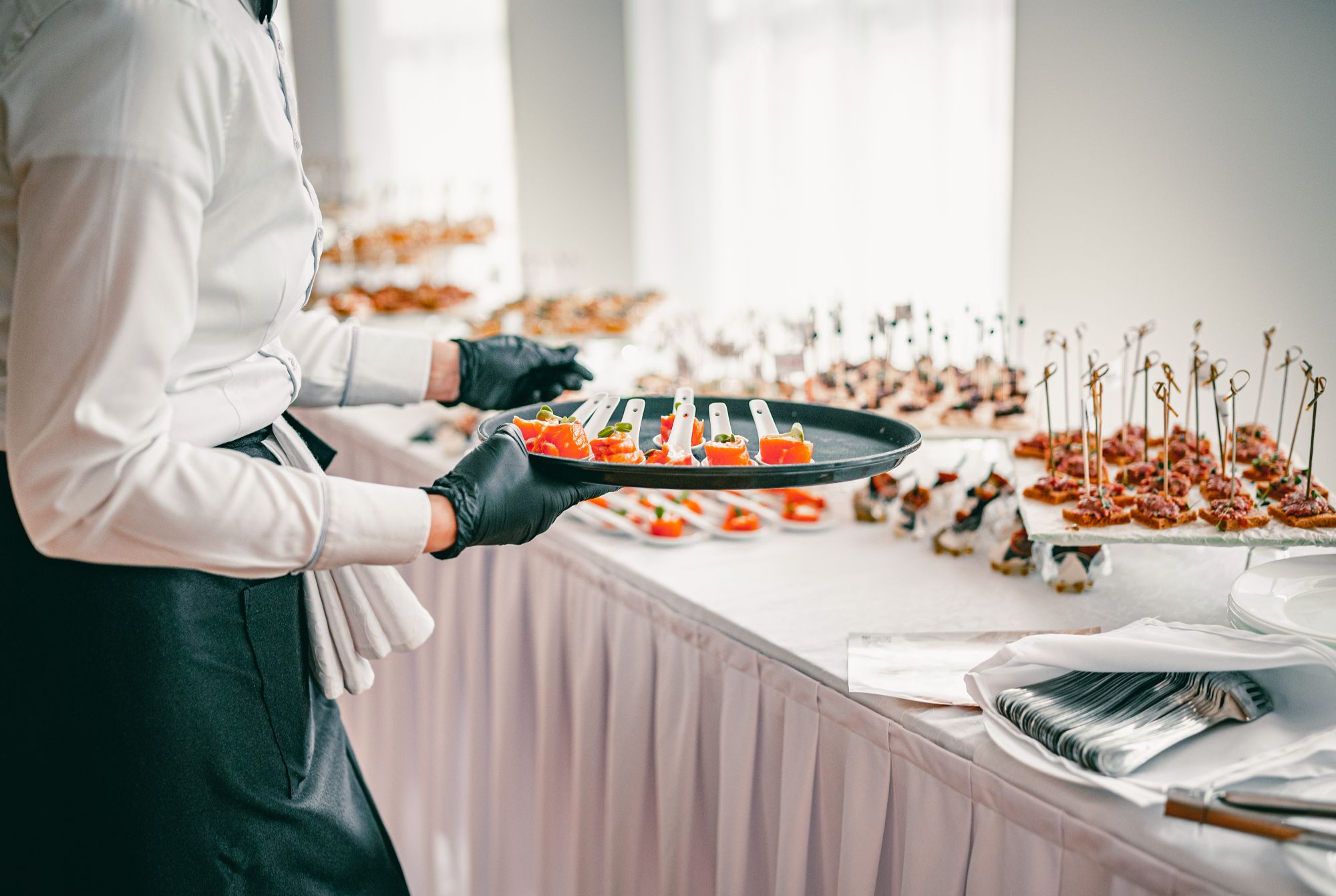 Kelner w rękawiczkach serwujący przekąski na eleganckim bankiecie przy stole z potrawami.
