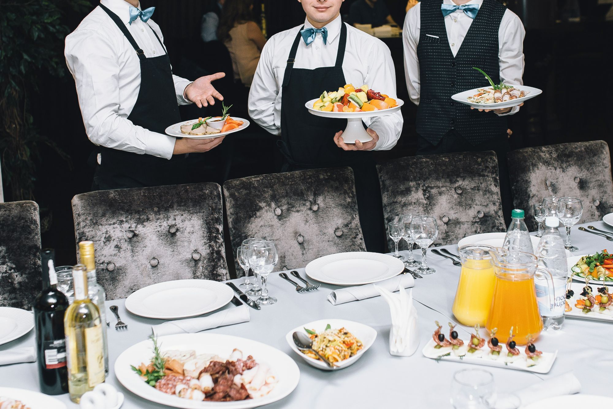 Kelnerzy serwujący różne potrawy na eleganckim stole w restauracji.