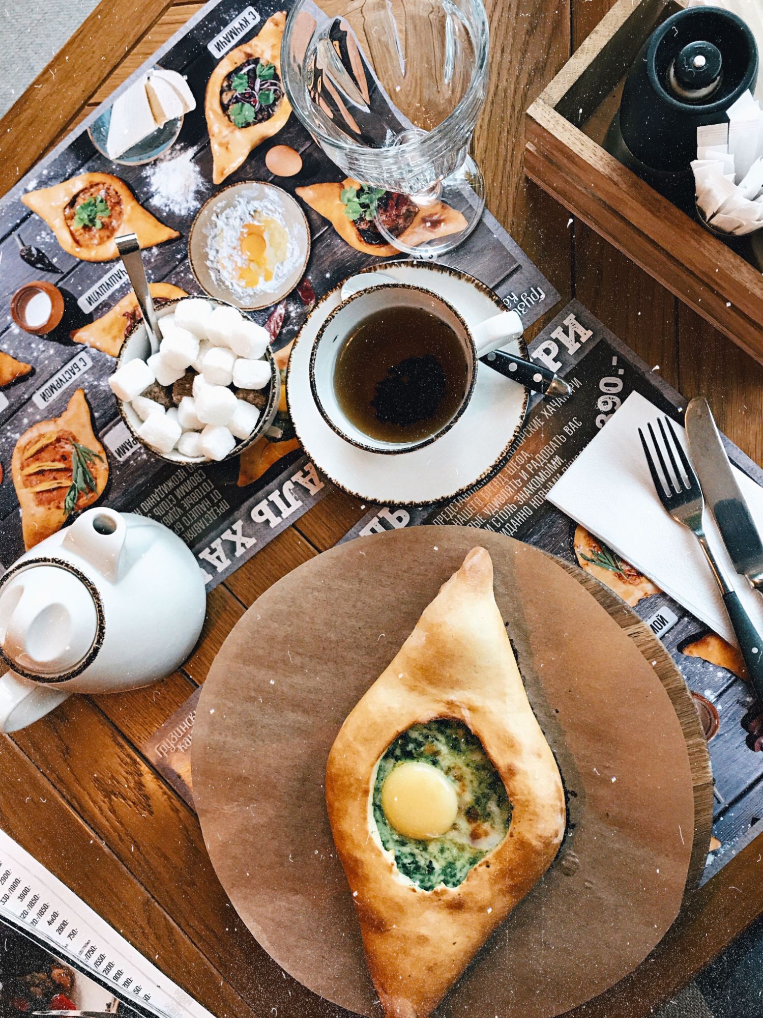 Stół z khachapuri, herbatą, cukrem i dodatkami w kawiarni na tle menu.