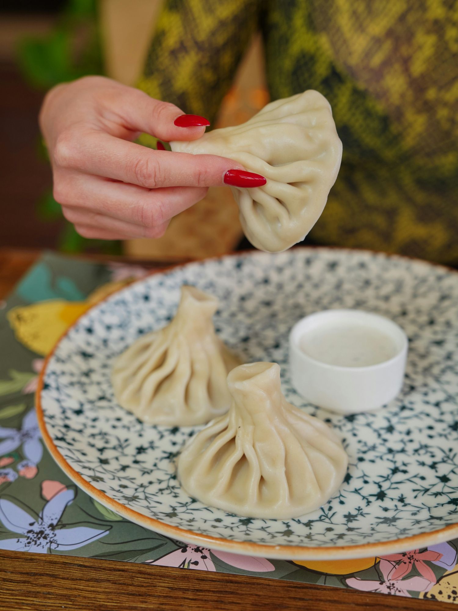 Kobieta trzyma pierożek na talerzu, obok znajduje się sos do dipowania i inne pierożki.
