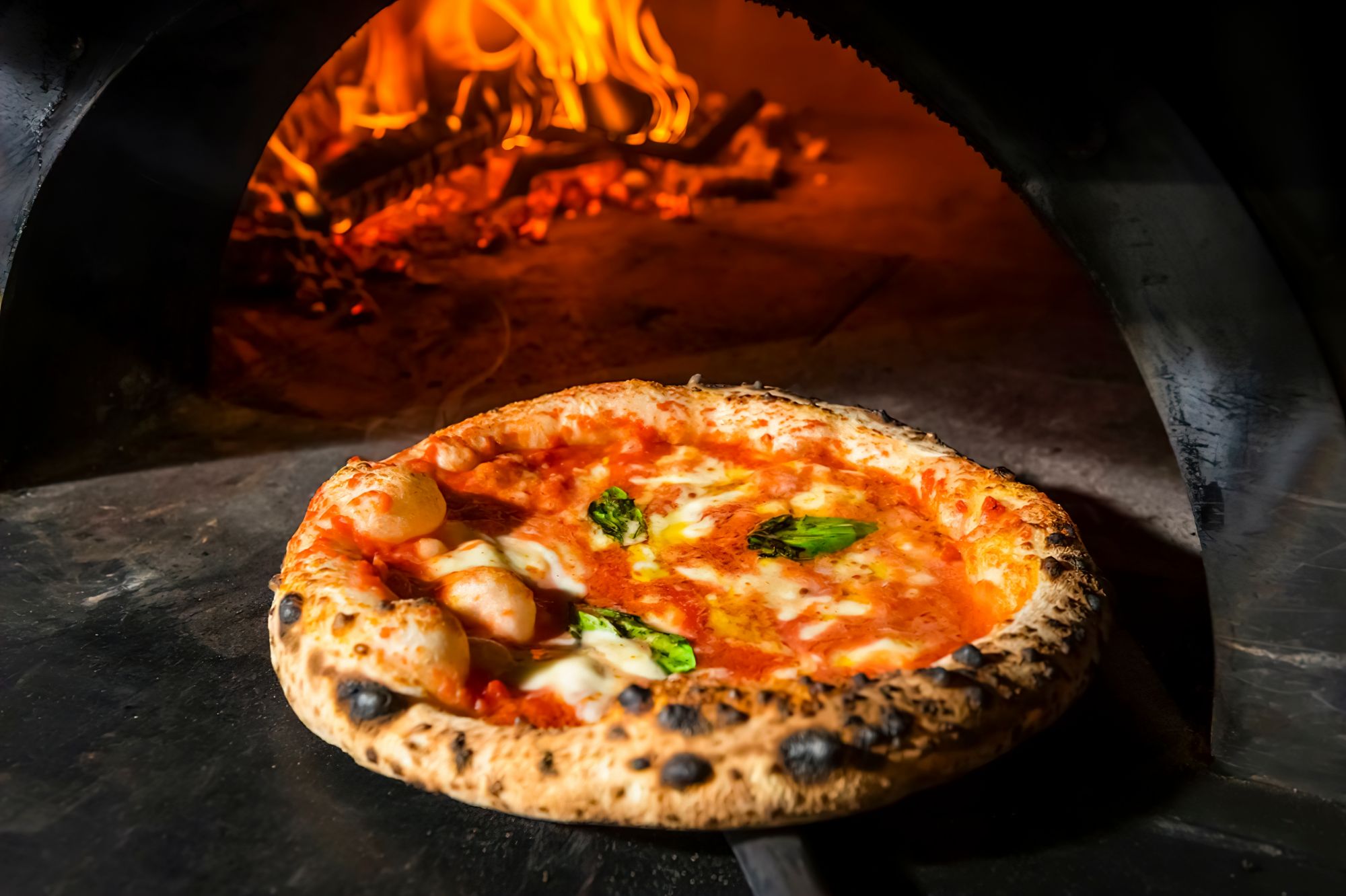 Pyszna pizza Margherita pieczona w piecu opalanym drewnem, z serem, sosem pomidorowym i świeżymi ziołami.