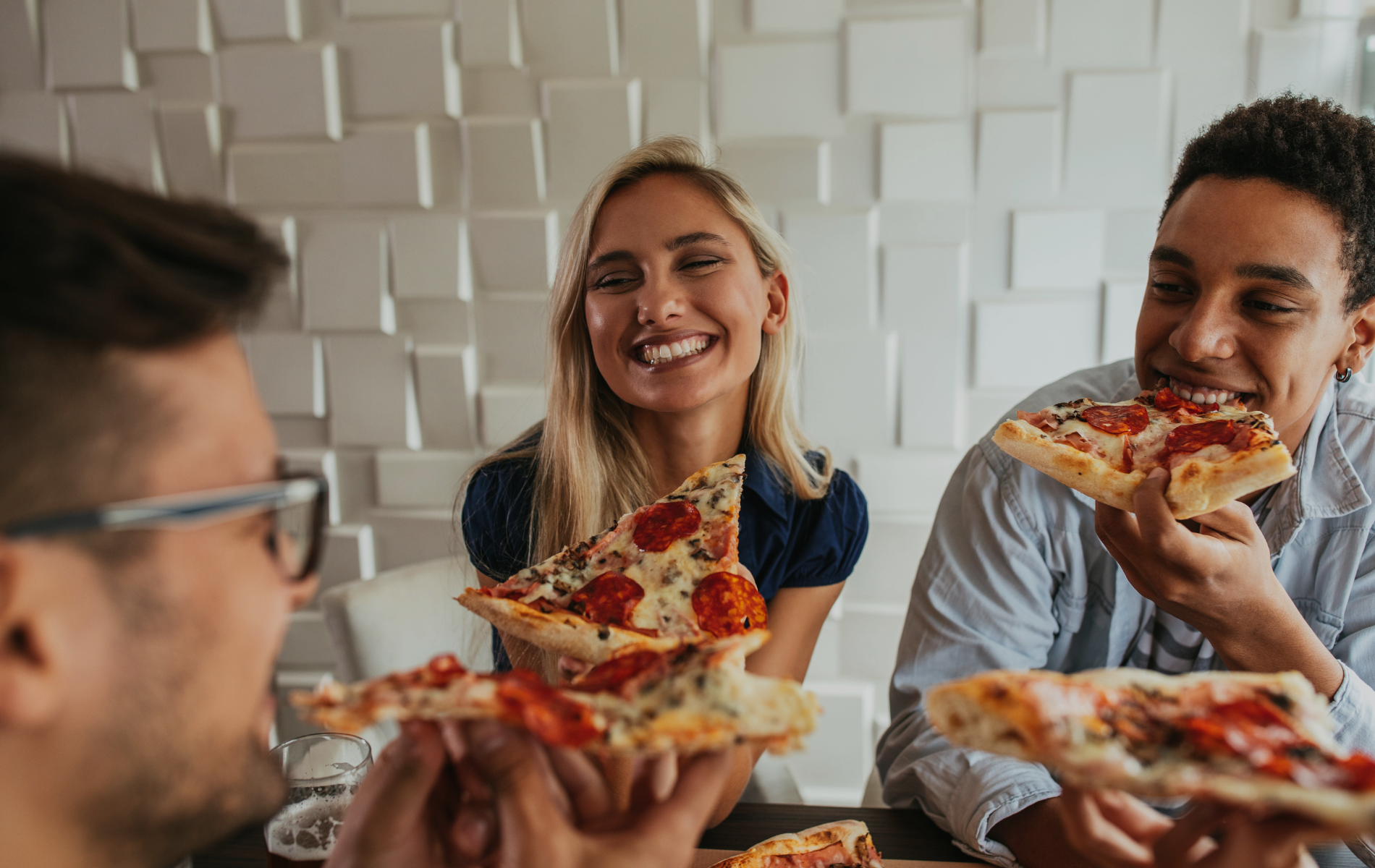Grupa prijatelja uživa u pizzi u suvremenom prostoru s dekorom od bijelih ploča.