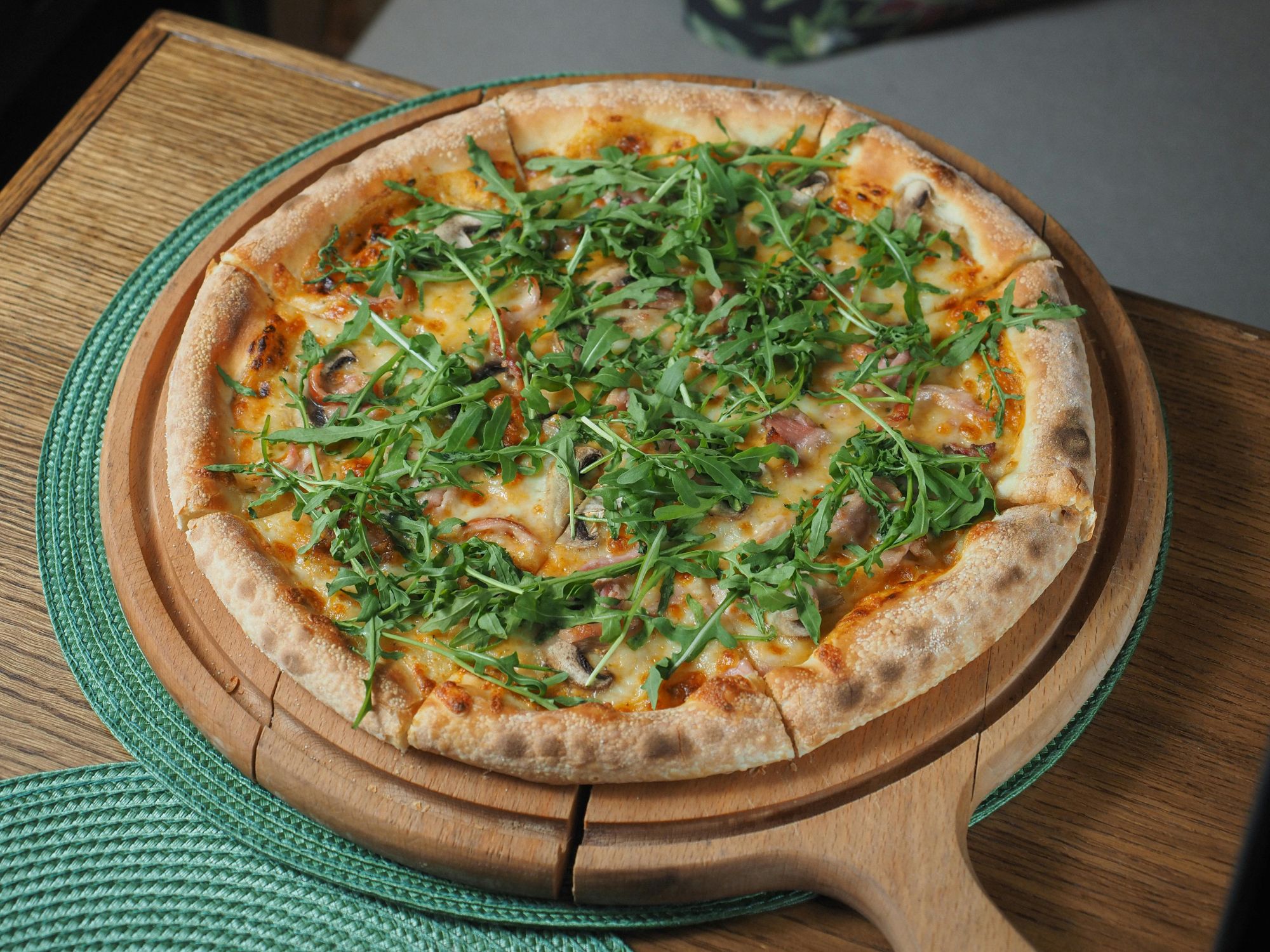 Pizza s sirom, šunpaj i svježom rukolom na drvenom pladnju.