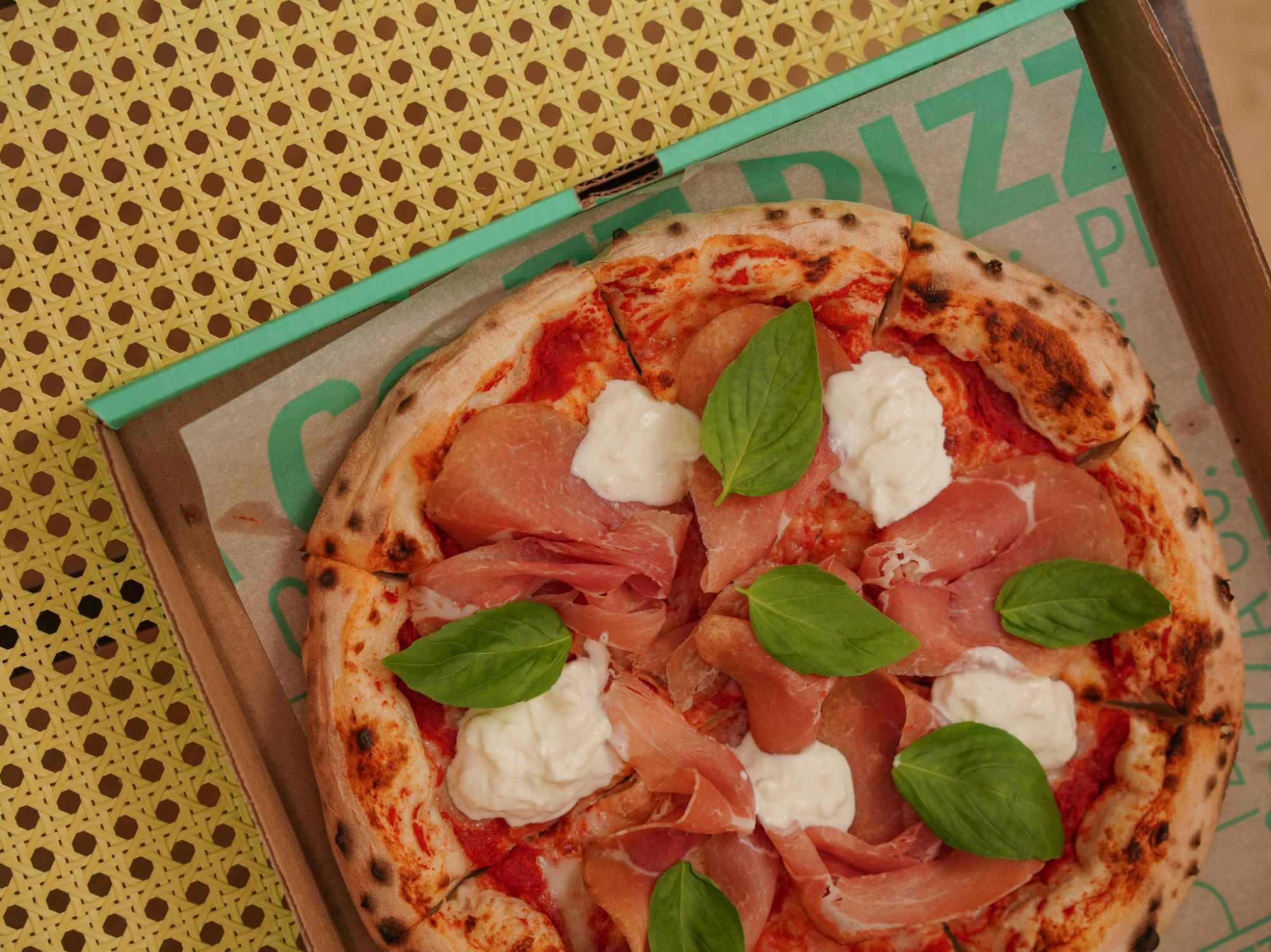 Pizza s pršutom, svježim bosiljkom i mozzarellom u kartonskoj kutiji.