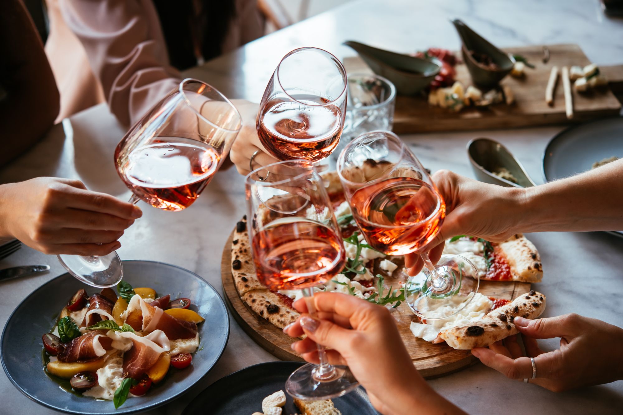 Vesela večera s pizzom i čašama rose dok se prijatelji druže za stolom.