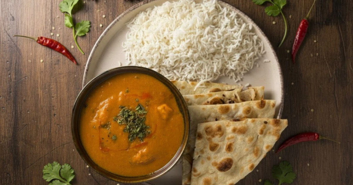 Talerz z ryżem, placuszkami naan i sosem curry z kurczakiem, przyozdobiony ziołami i papryczkami chili.