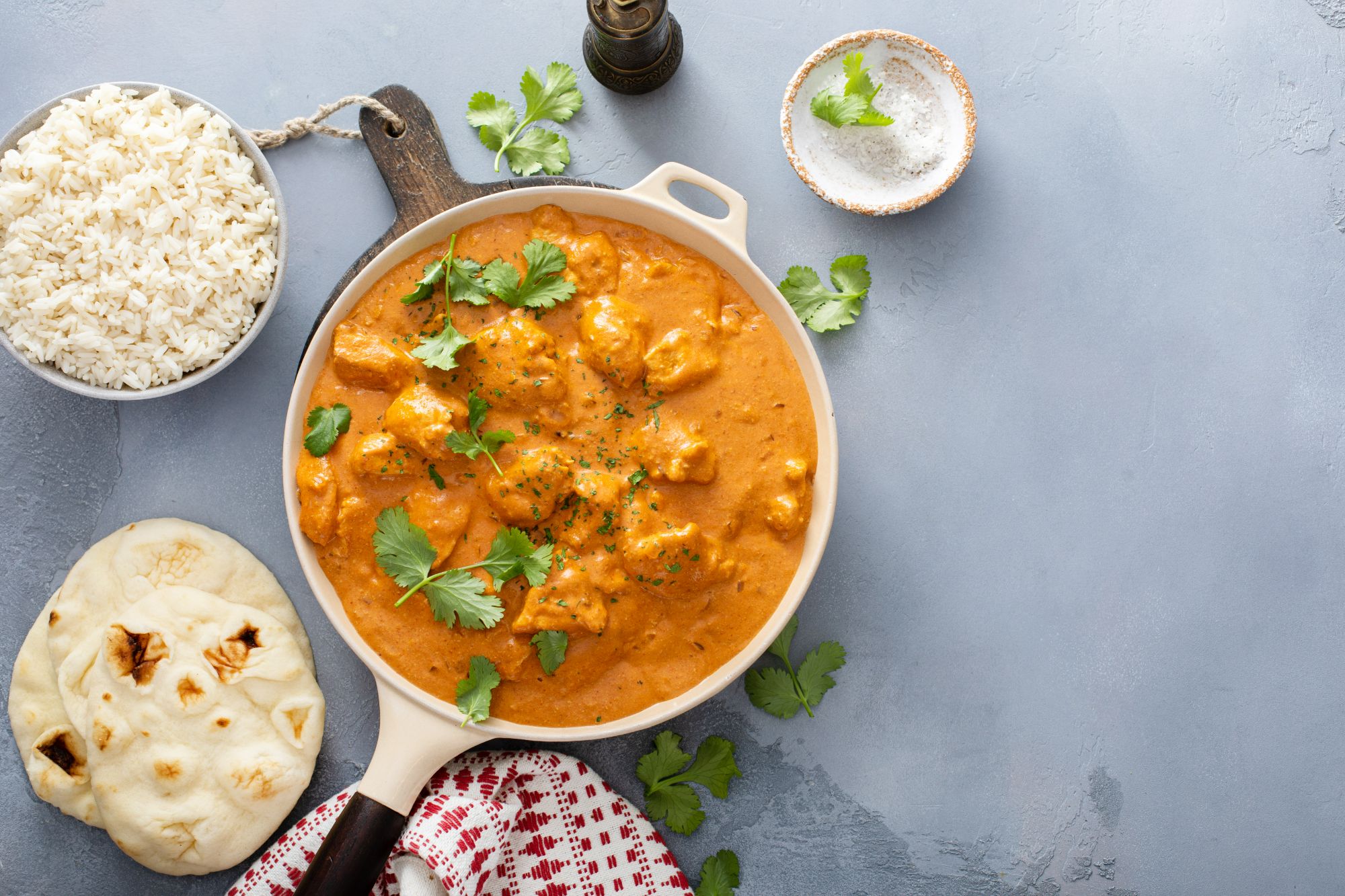Kurczak w sosie curry z świeżą kolendrą, ryżem i naanem, na szarej powierzchni.