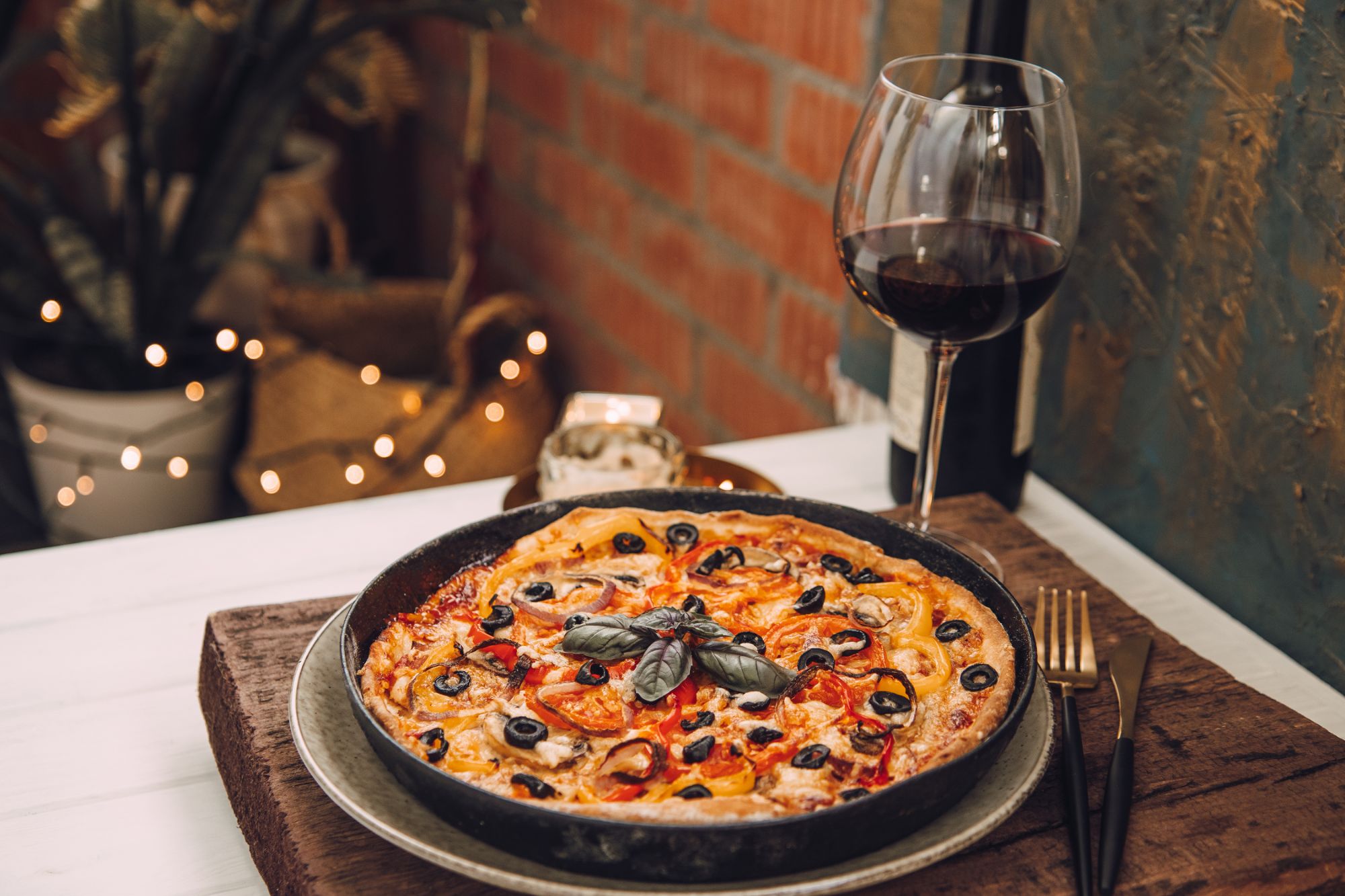 Pyszna pizza z czarnymi oliwkami i czerwoną papryką, podana z kieliszkiem czerwonego wina w klimatycznym otoczeniu.