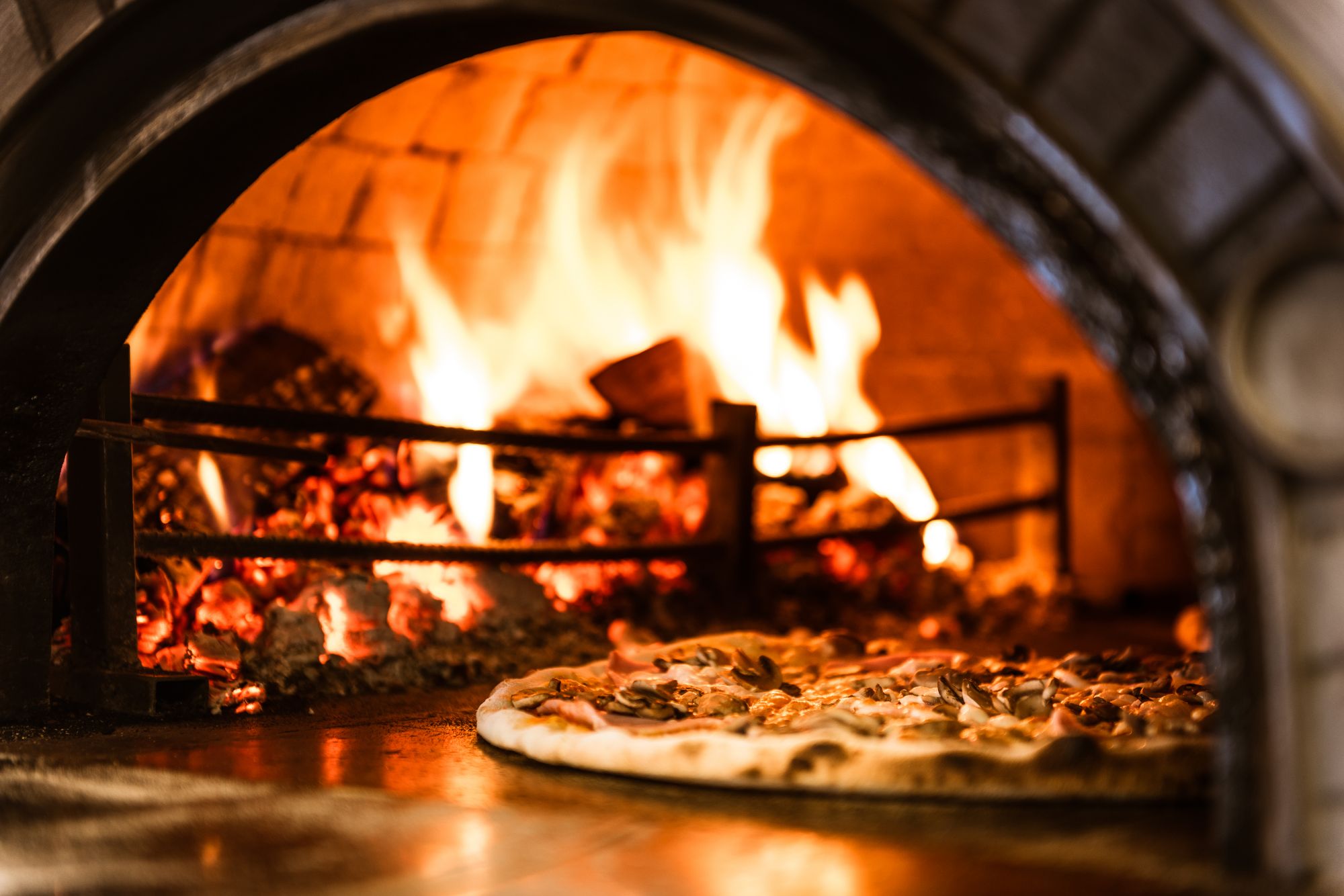 Pyszna pizza pieczona w tradycyjnym piecu opalanym drewnem, z płomieniami w tle.