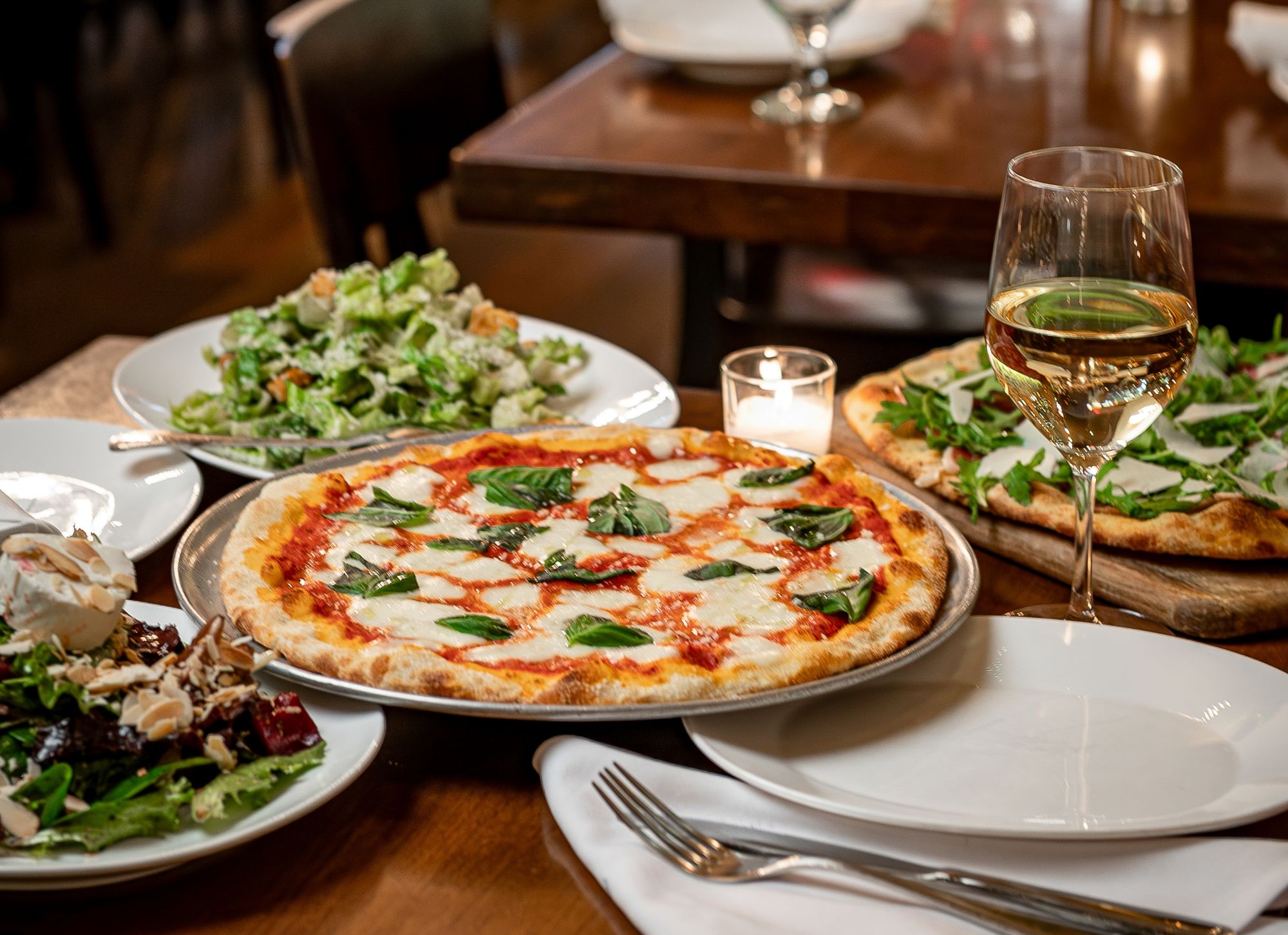 Pizza z bazylią, sałatka i lampka białego wina na stole w eleganckiej restauracji.