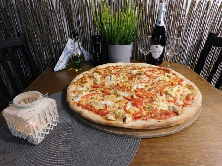 Pyszna pizza z serem, pomidorami i papryką na drewnianym stole, z butelką szampana i kieliszkami w tle.