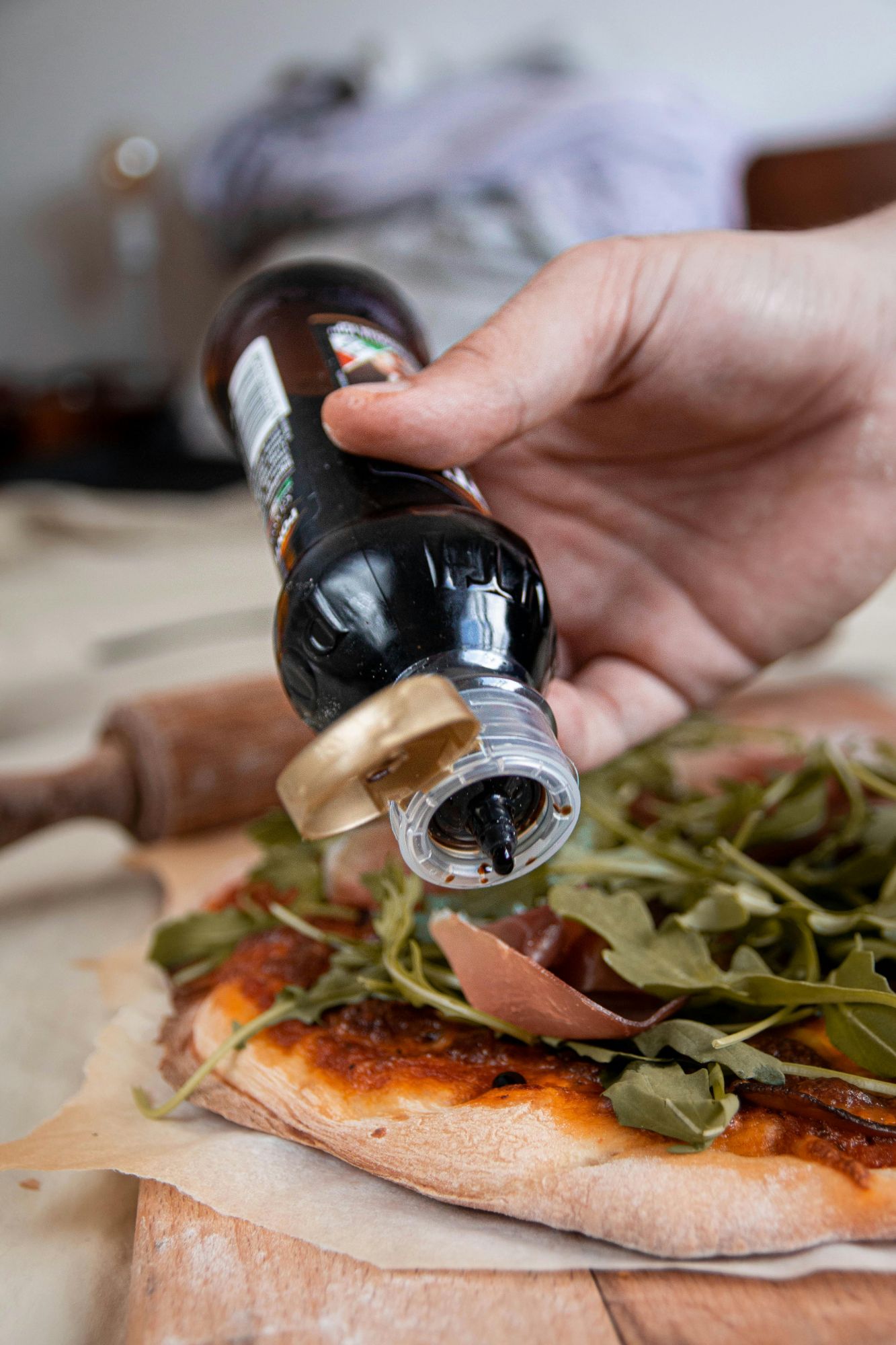 Osoba polewa świeżą pizzę sosem balsamicznym, na cieście znajdują się miniowe składniki.