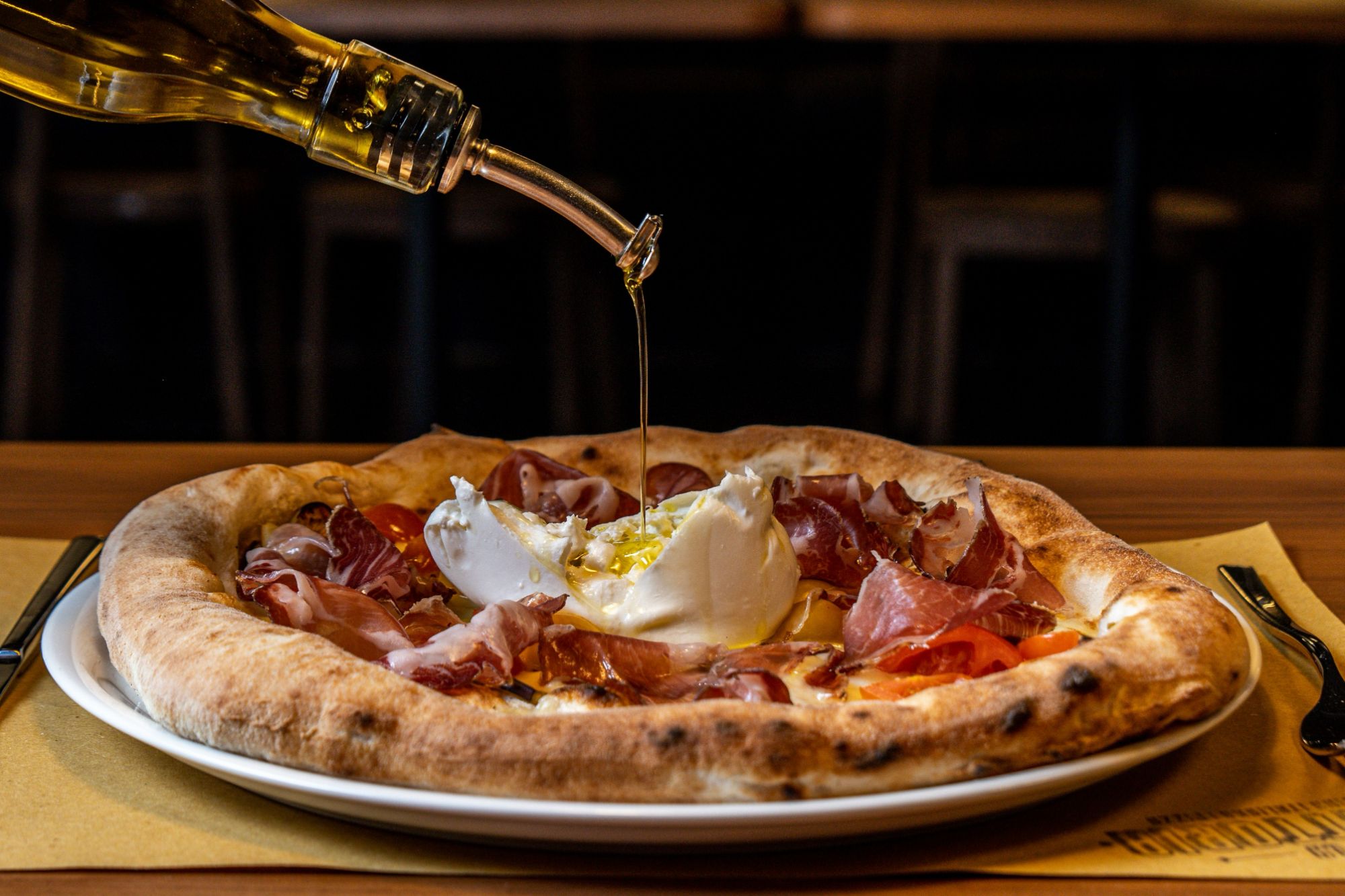 Pizza z serem burrata, szynką i oliwą, na talerzu w restauracji.