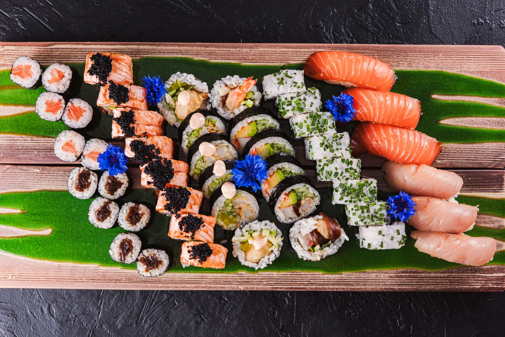 Taca sushi z różnorodnymi kawałkami sushi, w tym łososiem, warzywami i dekoracjami kwiatowymi.