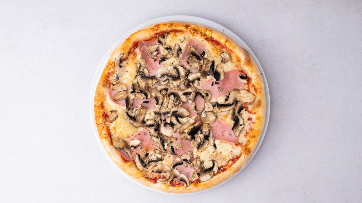 Pizza z szynką i pieczarkami na jasnym tle.