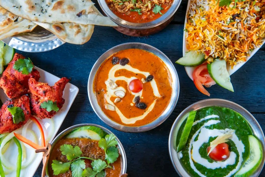 Różnorodne indyjskie dania, w tym curry, biryani, naan i sałatki, na niebieskim stole.