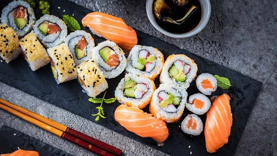 Sushi na talerzu, różne rolki z awokado, łososiem i warzywami, podane z sosem sojowym i pałeczkami.